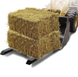 A farmer loads a round hay bale onto a tractor, preparing for transport in a rural landscape.